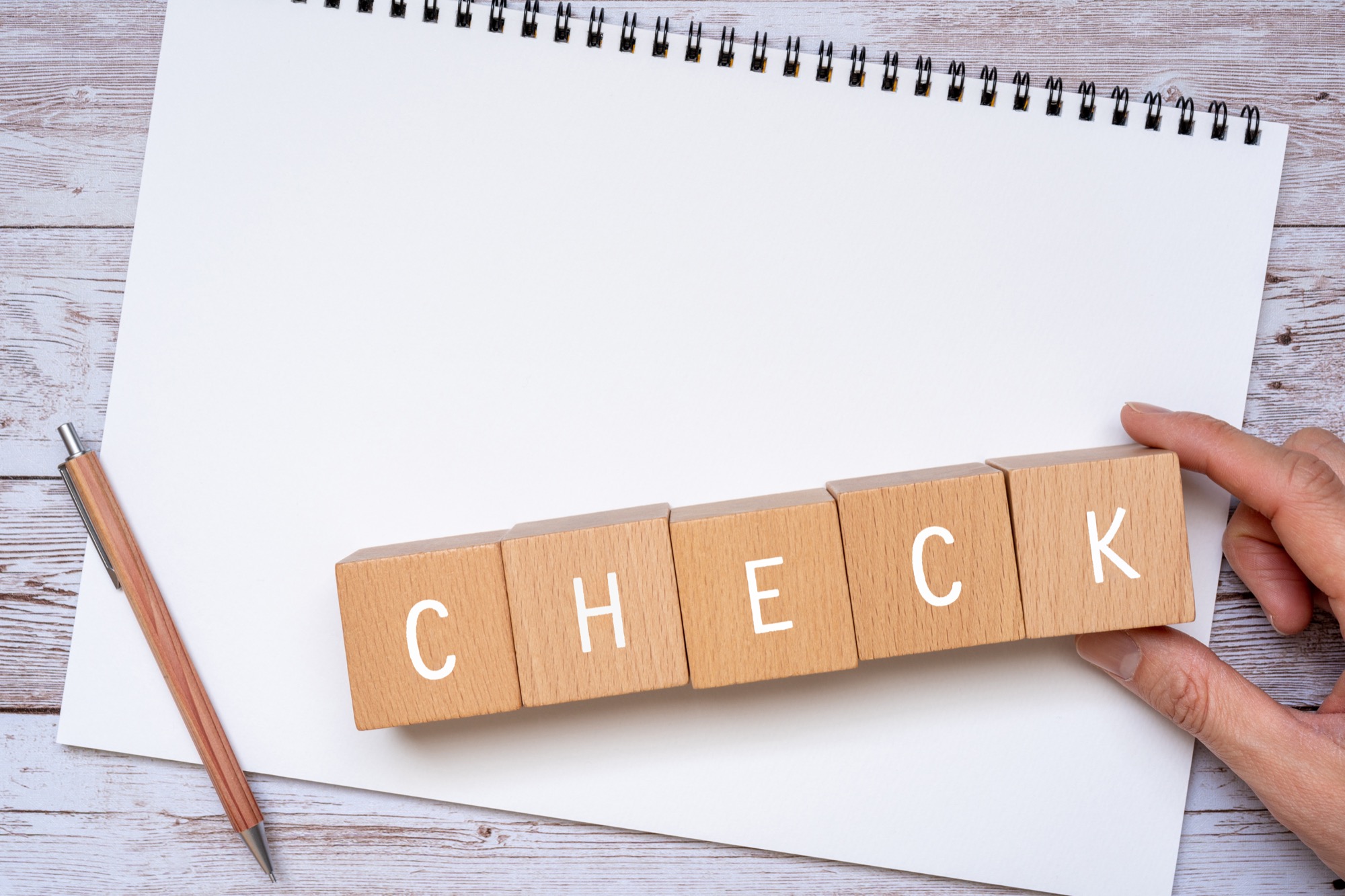 「CHECK」と書かれた積み木、ノート、ペン、人の手