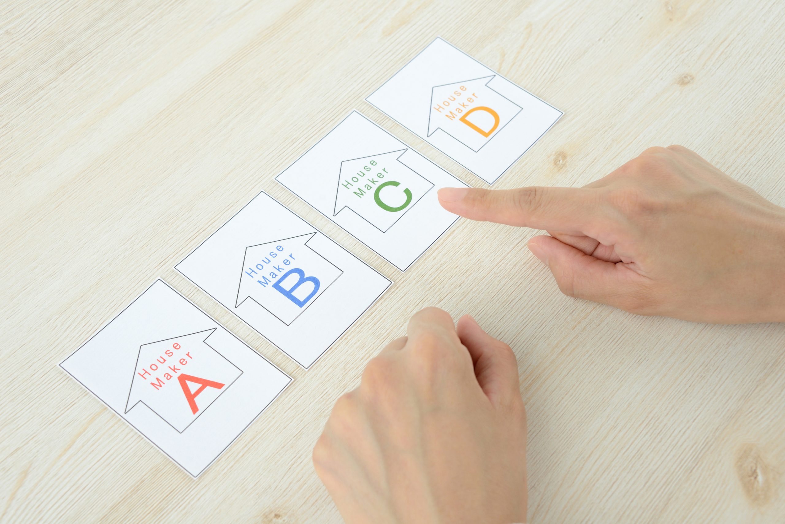 木目調のテーブルに並べられた4枚の住宅メーカーのカード(A, B, C, D)