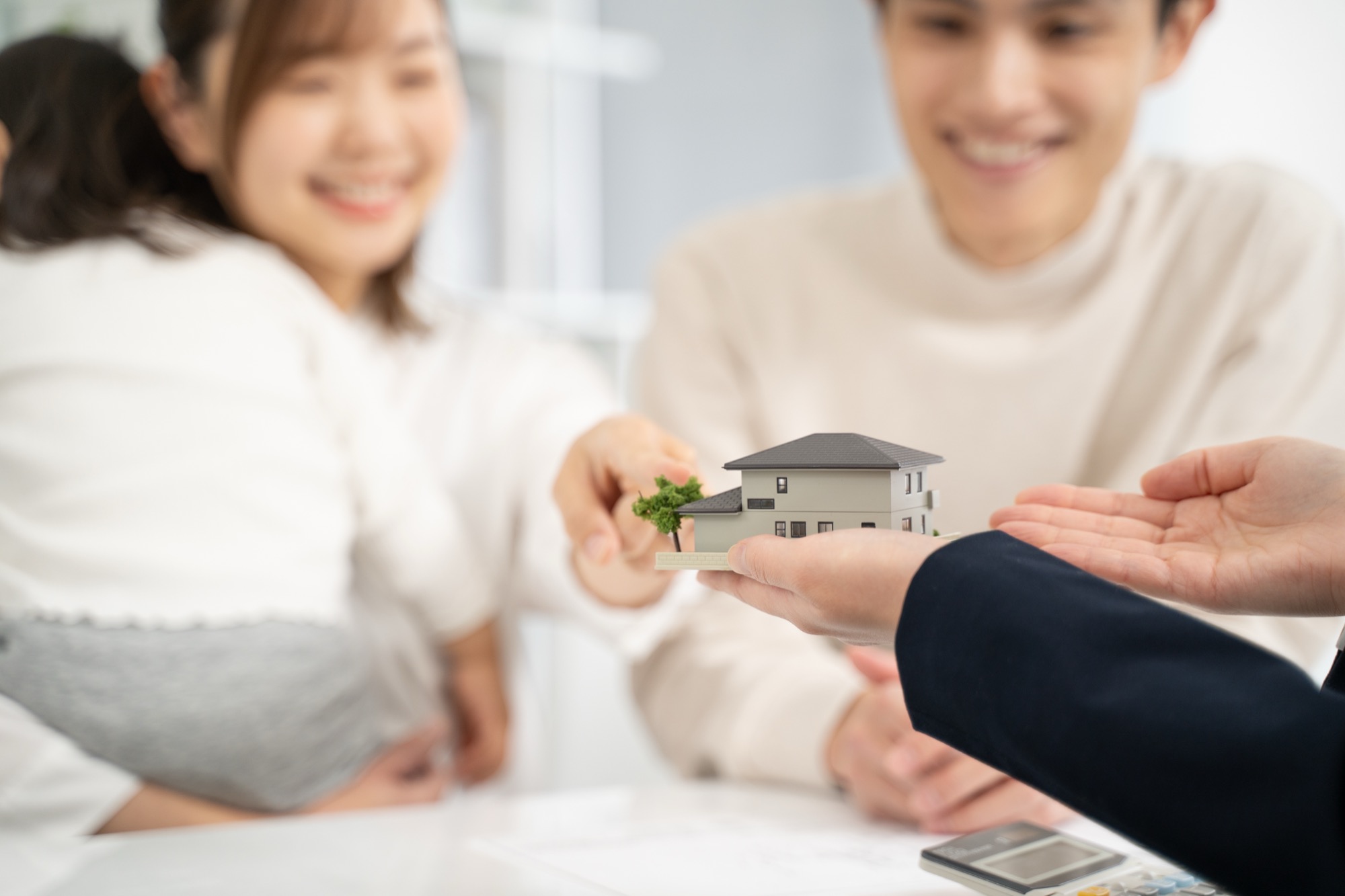家の模型を持って設計の話をするビジネスウーマンと家族