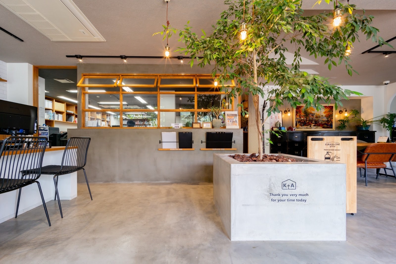 モダンなオフィス内装の施工事例。モルタル床とコンクリート壁、大きな観葉植物、木製窓枠が特徴。インダストリアルと自然が融合した、開放的で洗練された空間デザイン。