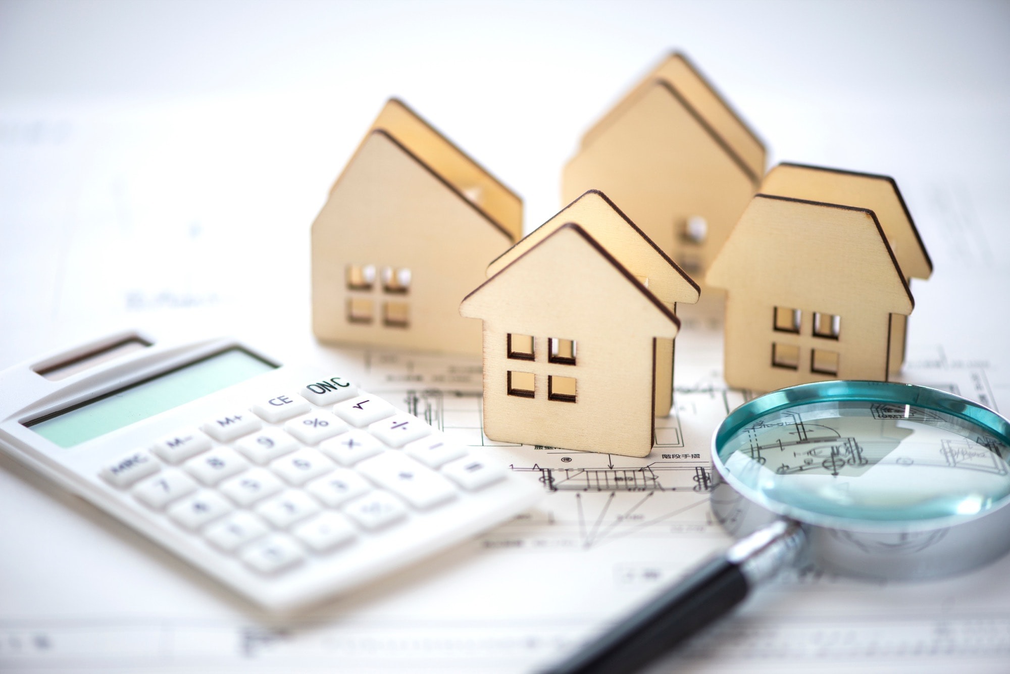 住宅の図面の上に、住宅模型と電卓、虫眼鏡を置き、住宅価格についてのイメージを伝える写真。