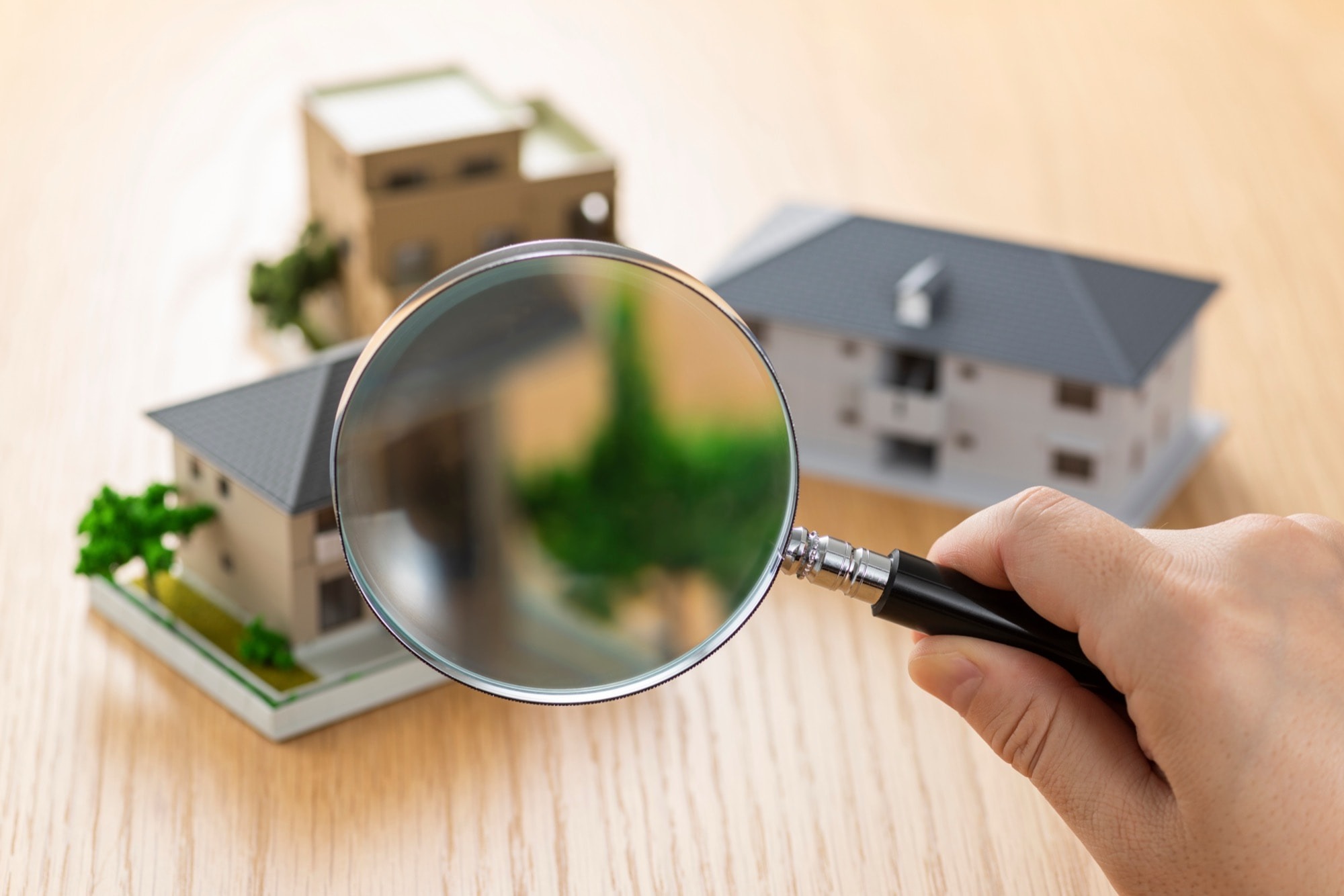虫眼鏡を持って家の模型を観察する人